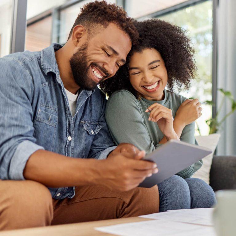 Happy couple sitting on couch, reviewing their finances, looking for ways to build wealth.