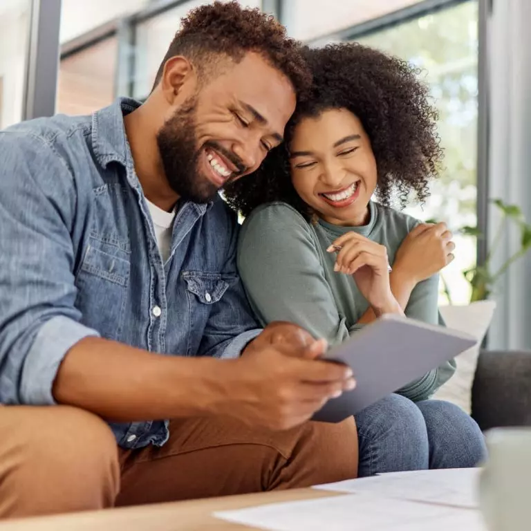 Happy couple sitting on couch, reviewing their finances, looking for ways to build wealth.