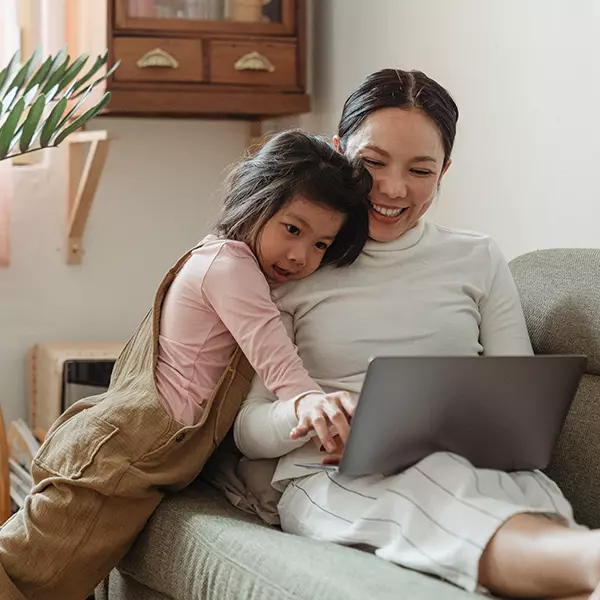 A woman views her estate plan and will on her tablet will sitting on her couch with her young daughter.