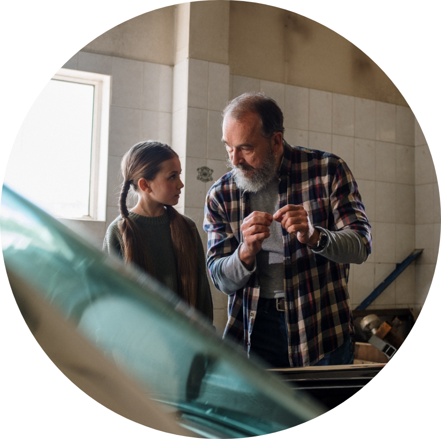 A girl with pigtails and her grandfather talk in the garage.