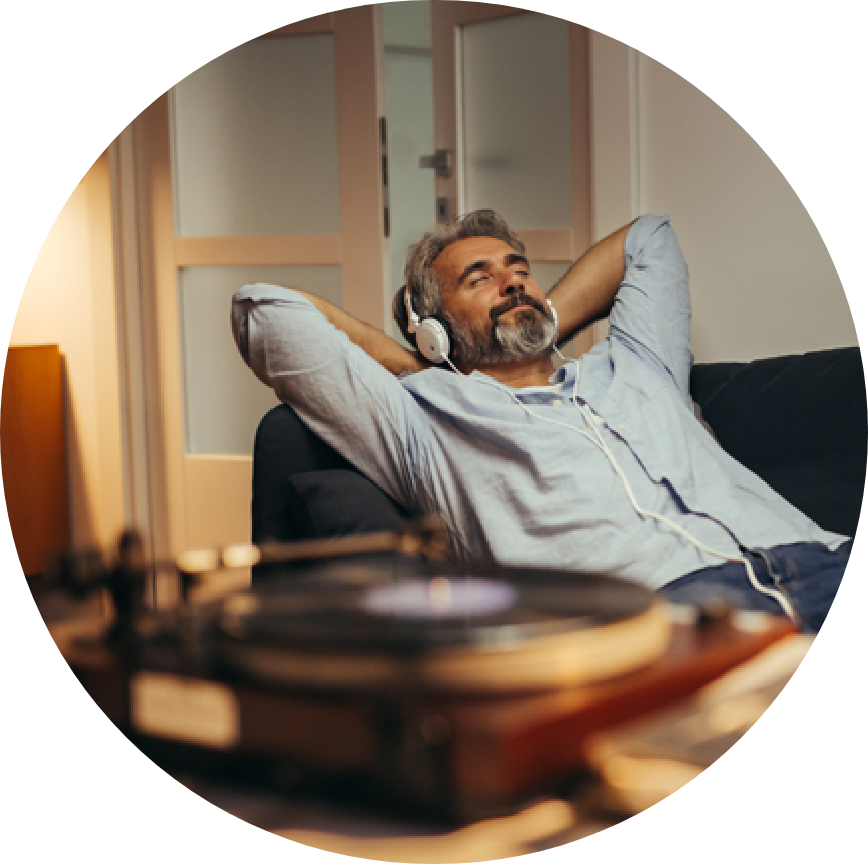 A bearded man wearing headphones reclines comfortably on a brown leather sofa.
