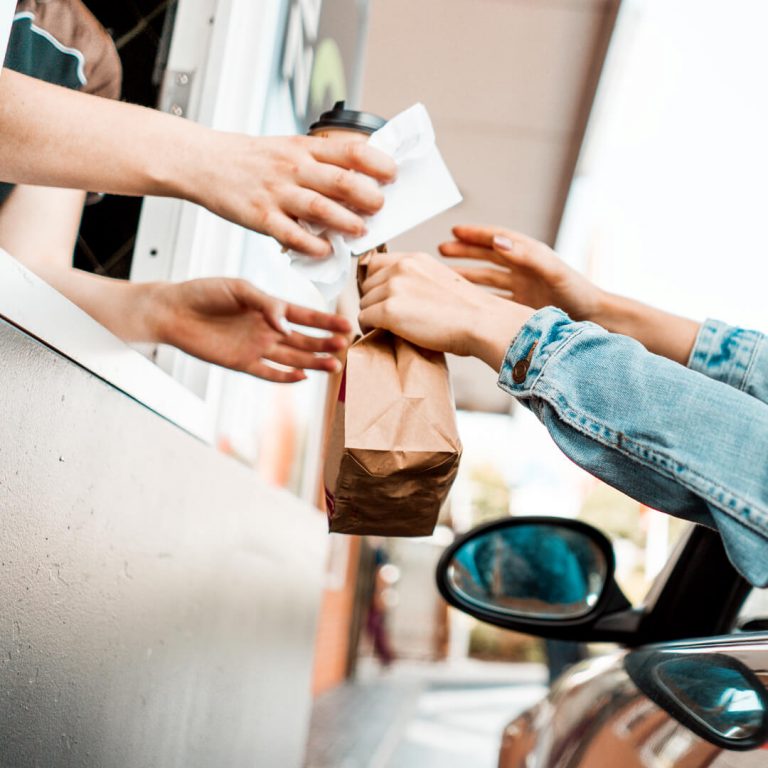 Fast food attendant handing fast food and coffee to driver in car (two items that can eat into a budget).