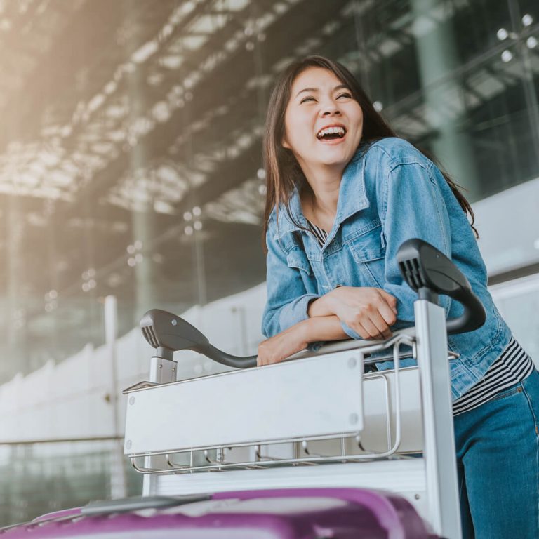 Young woman smiling in airport terminal with her luggage.