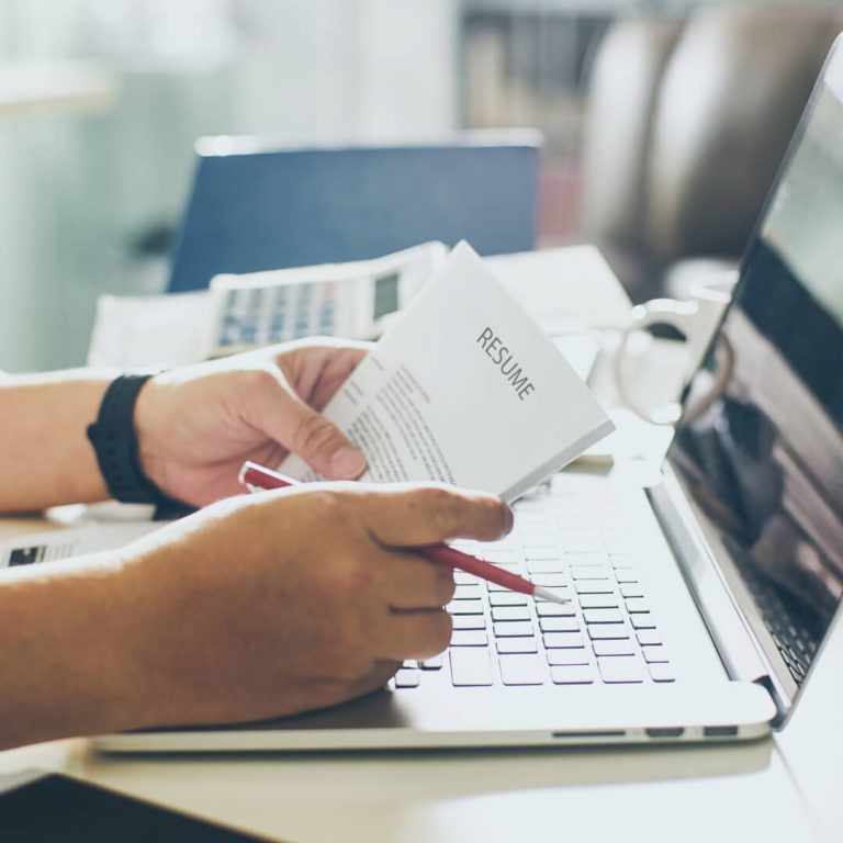 Hands holding a resume over a computer keyboard.
