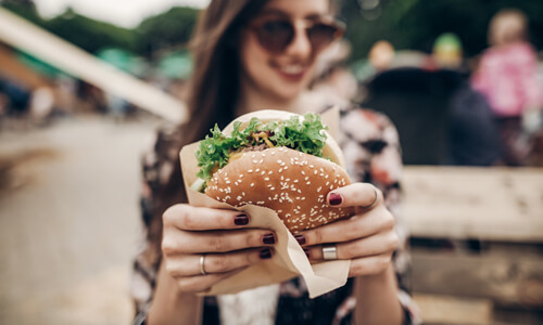 Woman smiling and holding a burger at an outdoor restaurant.