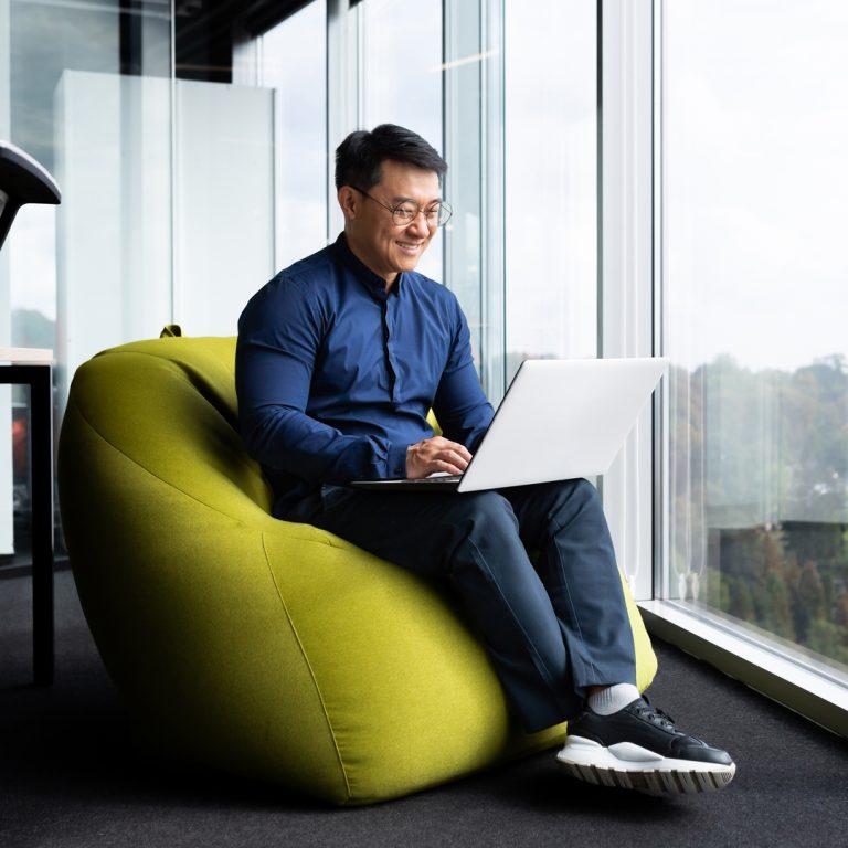 Man sits on large yellow cusion at office, illustrating career cushioning concept