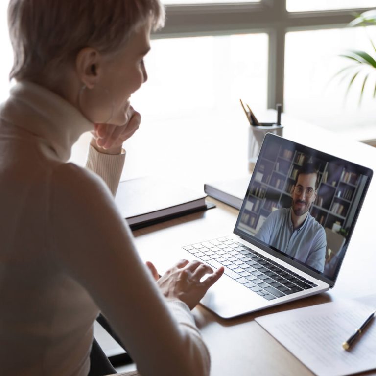Woman attending virtual job fair, speaking with man via teleconferencing app on her laptop.