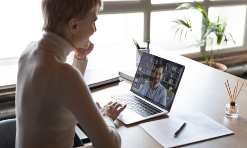 Woman attending virtual job fair, speaking with man via teleconferencing app on her laptop.