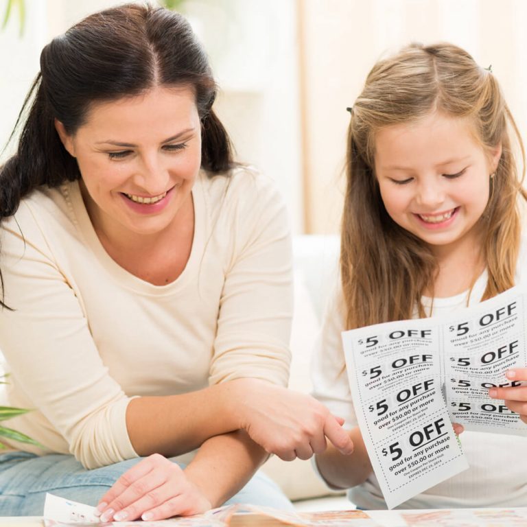 Mother and daughter clipping coupons together, smiling and saving money.