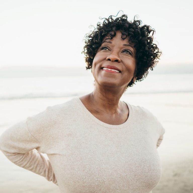 Smiling woman outdoors on beach contemplating retirement