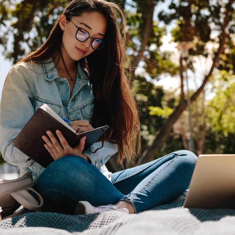 College student sitting outdoors with her laptop and schoolbooks.