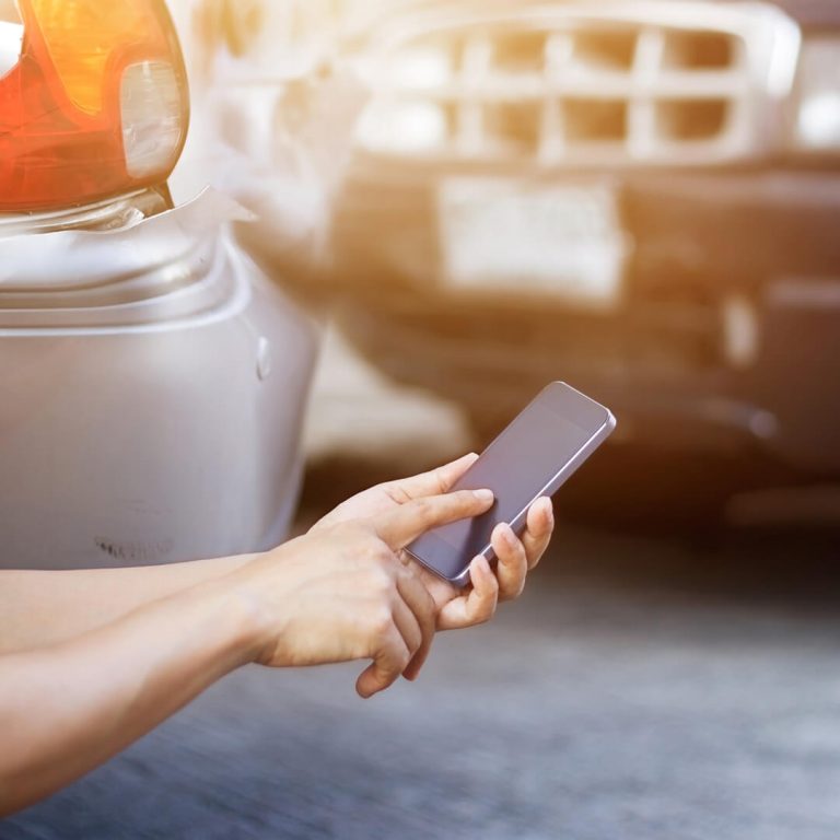 closeup of mobile phone with car collision in the background.