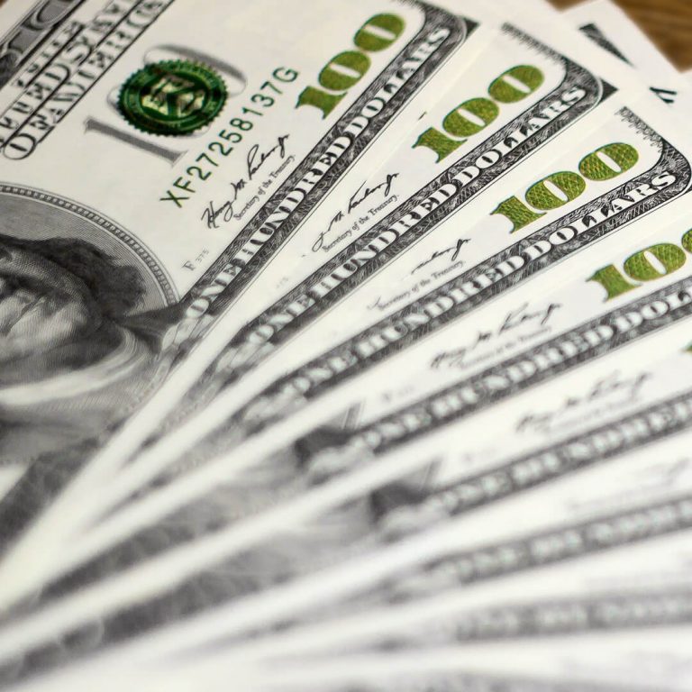 A stack of hundred dollars bills on a table.