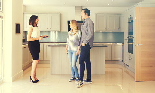 Young couple looking to buy a home standing in new kitchen with realtor.