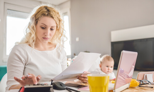 Concerned mother crunching daycare costs with young baby in background.