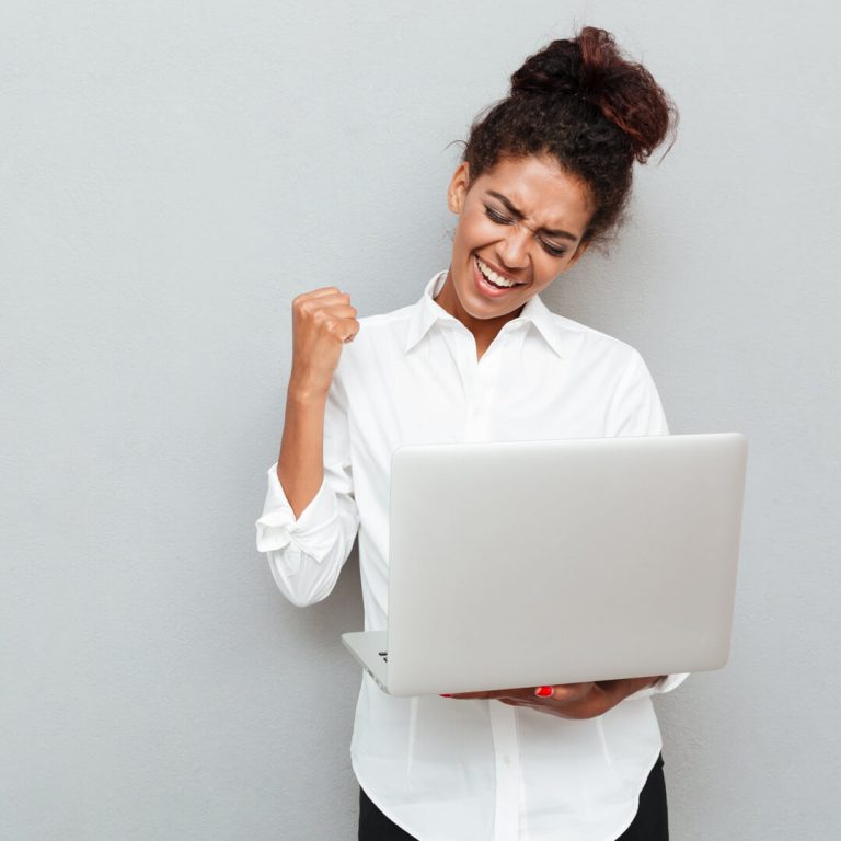 Woman holding laptop in hand and cheering because her direct deposit came through.