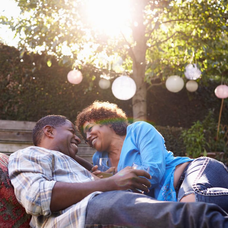 Retired couple in backyard drinking wine, embracing and laughing.