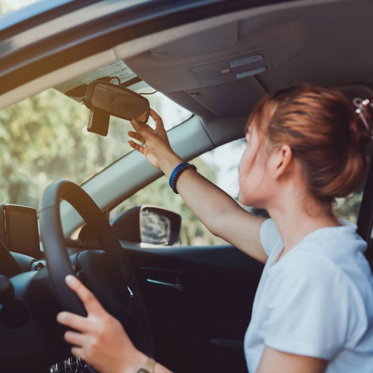 Young woman practicing defensive driving and adjusting her rearview mirror.