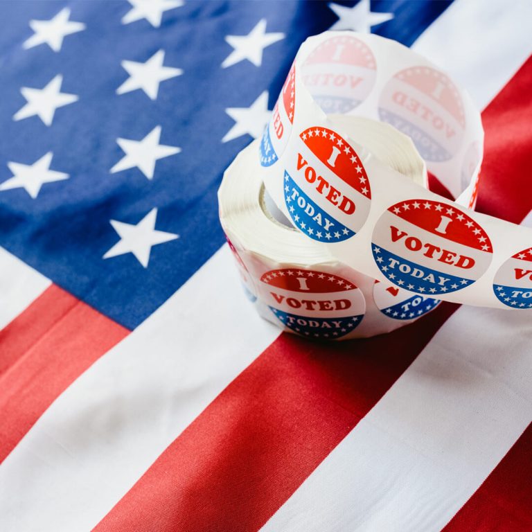 "I voted" stickers resting on top of American Flag, signifying Election Day.
