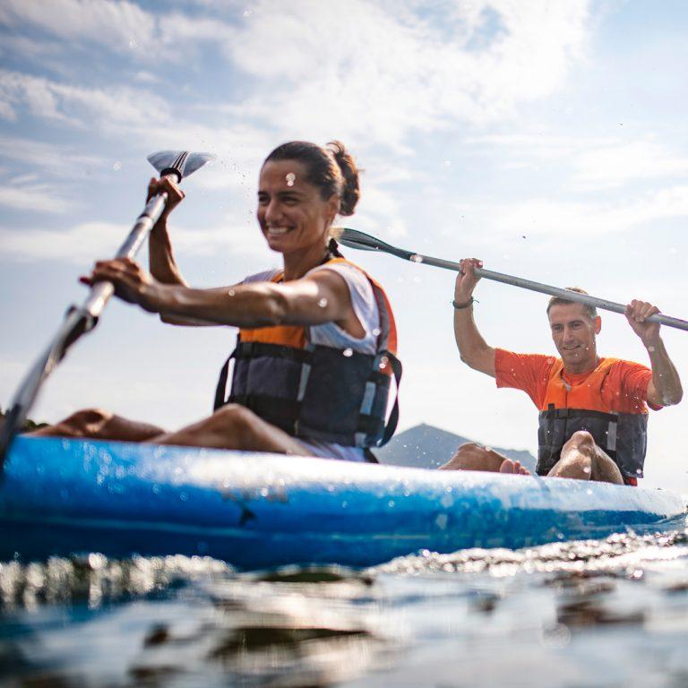 Energetic male and female kayakers in 40s paddling past camera; FIRE movement.