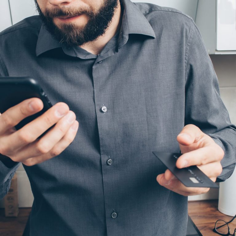 Man holding mobile phone in one hand, a gift card in the other due to a scam.