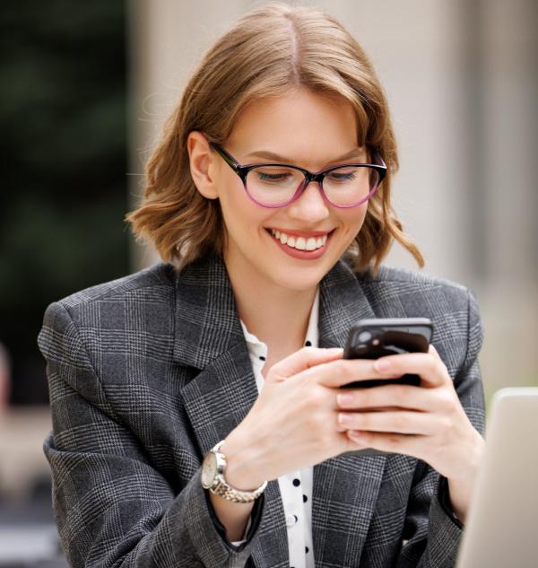 Young woman smiling viewing her cell phone as she manages her debt using Balance.