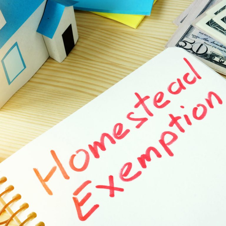 Notepad with "Homestead Exemption" written on it - model house and dollar bills also on desk.
