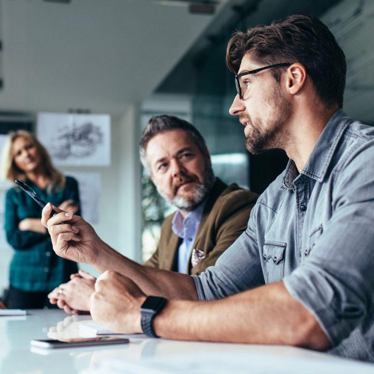 Employee speaking at conference table, with fellow employees listening to him.