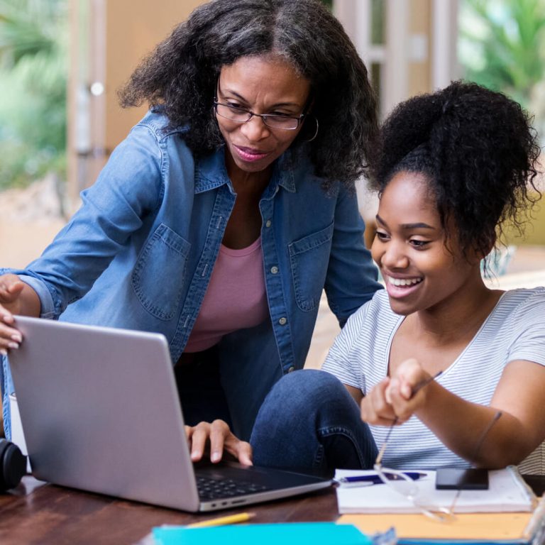 Mother helping her adult daughter review her finances at kitchen table.