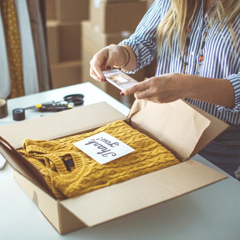Woman packing up gently-used sweater in a packing box, shipping it to buyer.