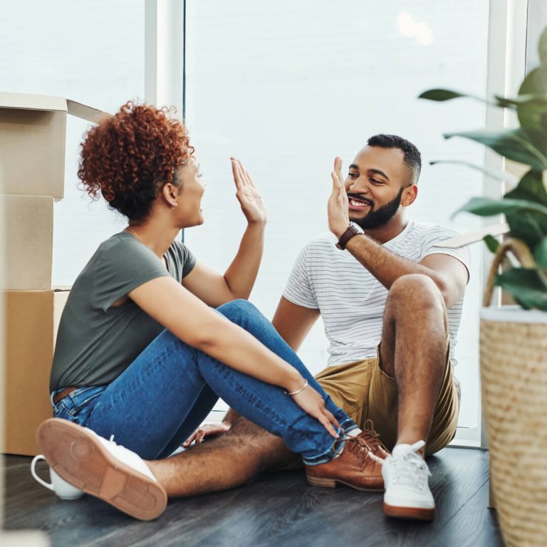 Couple sitting on floor, high-fiving each other, after successfully moving.