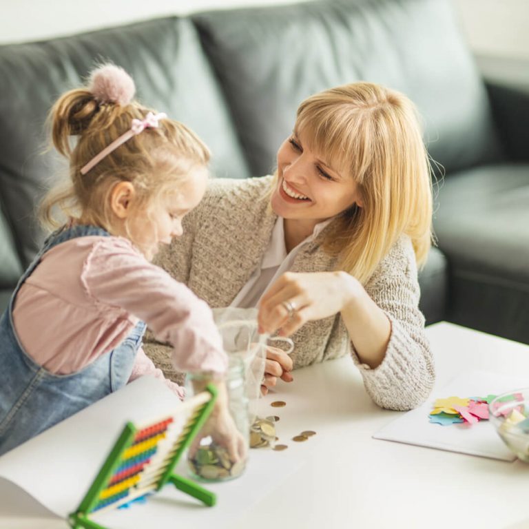 Mother and young daughter seated in living room, putting change into a jar.