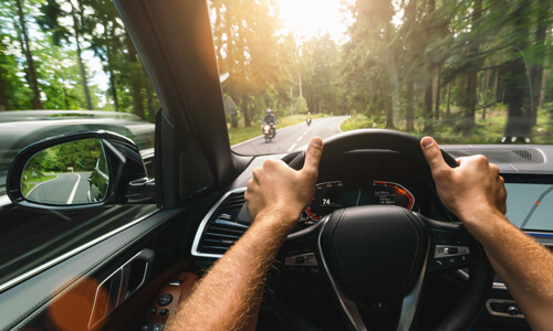 Hands on classic car steering wheel, driving on forest road.