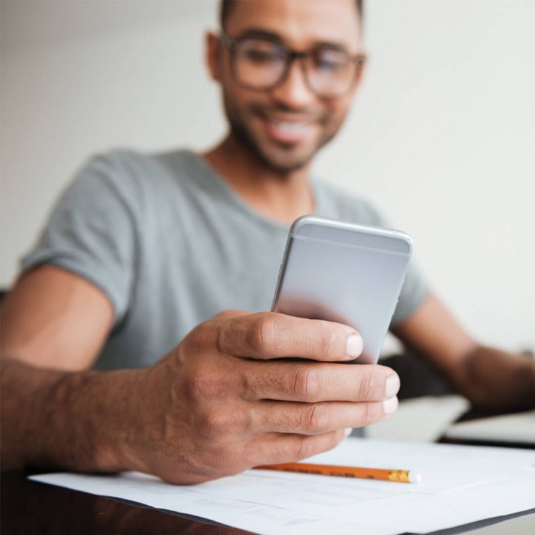 Man on laptop and mobile device, smiling because his check just cleared.