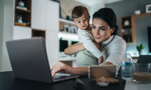 Mother holding young baby looking at computer screen at night.