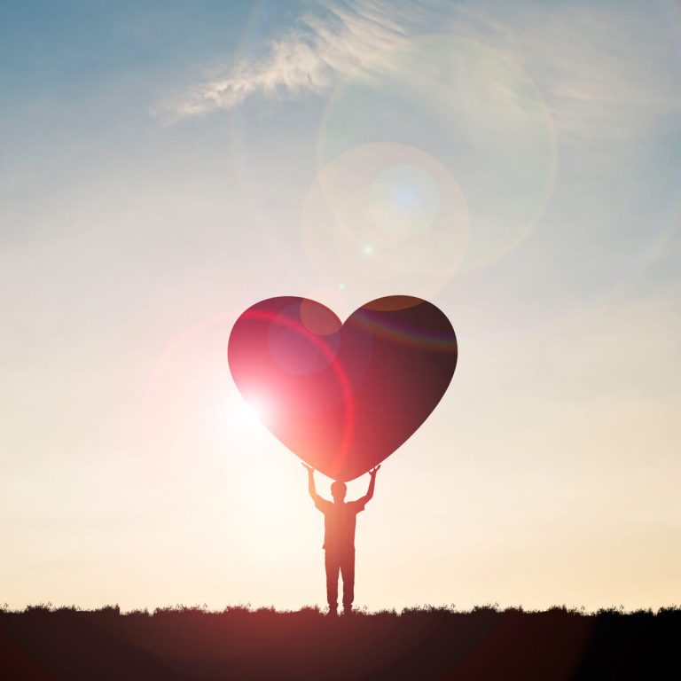 Silhouette of man at sunset holding a giant heart, illustrating philanthropy.
