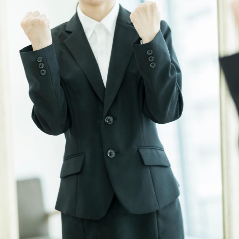 Happy woman stands in front of mirror in business clothes, happy she saved money on her wardrobe.