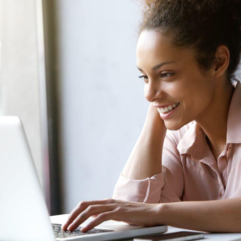 Woman smiling at desk looking at her computer screen.