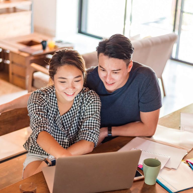 Couple seated at table looking at laptop, smiling.