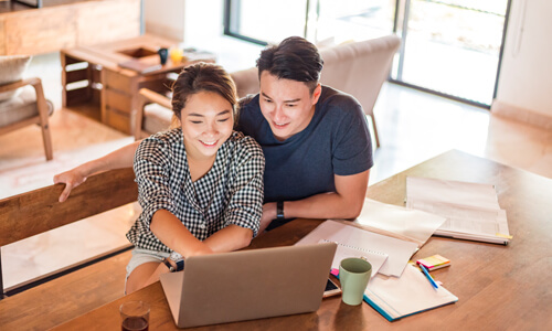 Couple seated at table looking at laptop, smiling.