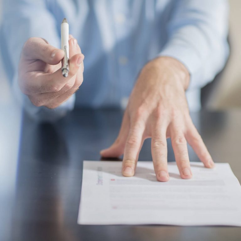 Closeup of hands pushing a document towards the camera for signature.