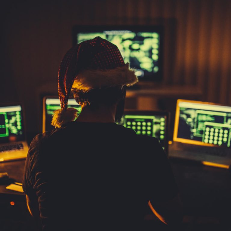 Scammer wearing santa hat looking at computer screens.