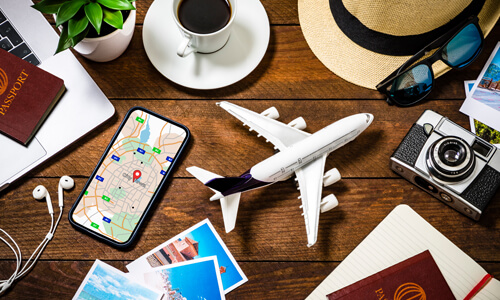 Items on table, representing a summer vacation: passport, phone, camera, sunglasses, hat, model airplane.