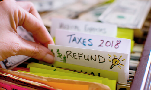 Closeup of filing cabinet with hand pulling up a tab that says "refund."
