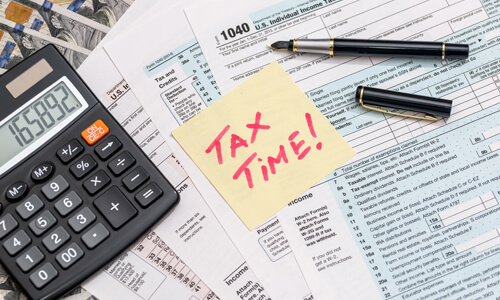 Various tax documents on desk, calculator, forms, post-it note that says "Tax time!"