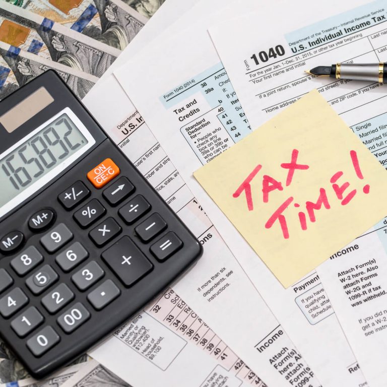 Various tax documents on desk, calculator, forms, post-it note that says "Tax time!"