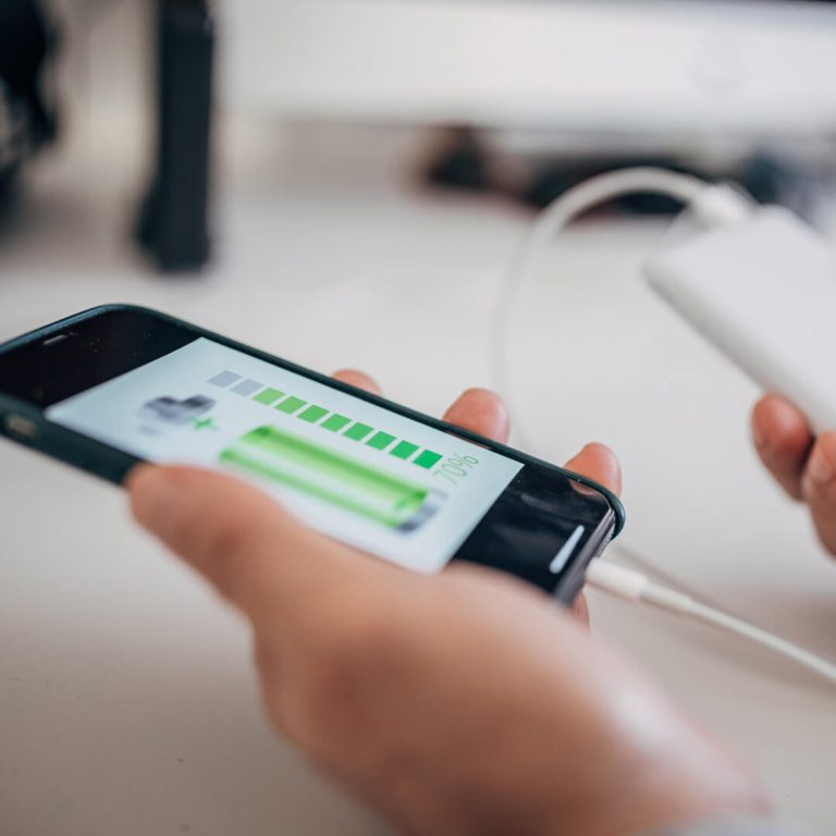 Hands charging a mobile device with a portable power device, a way to stay cybersafe when traveling.