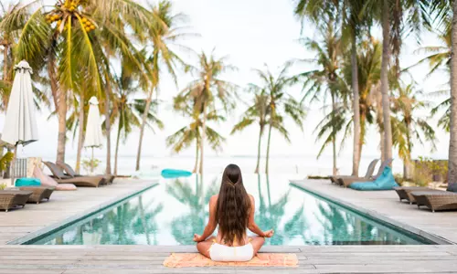 Woman on wellness retreat, doing yoga at resort pool.