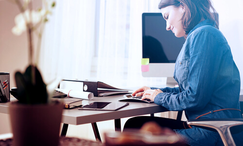 Woman at desk, smiling, working on taxes, entering numbers into a calculator.