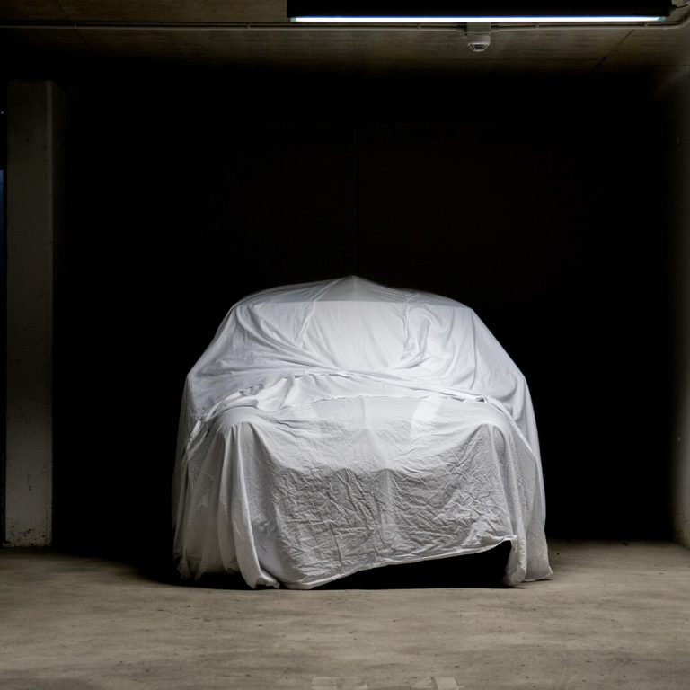 Classic car in garage, under protective cover.